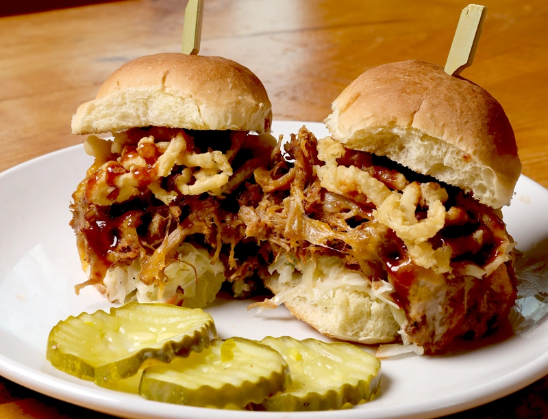 2 pulled pork sliders on a white plate with 3 pickle slices