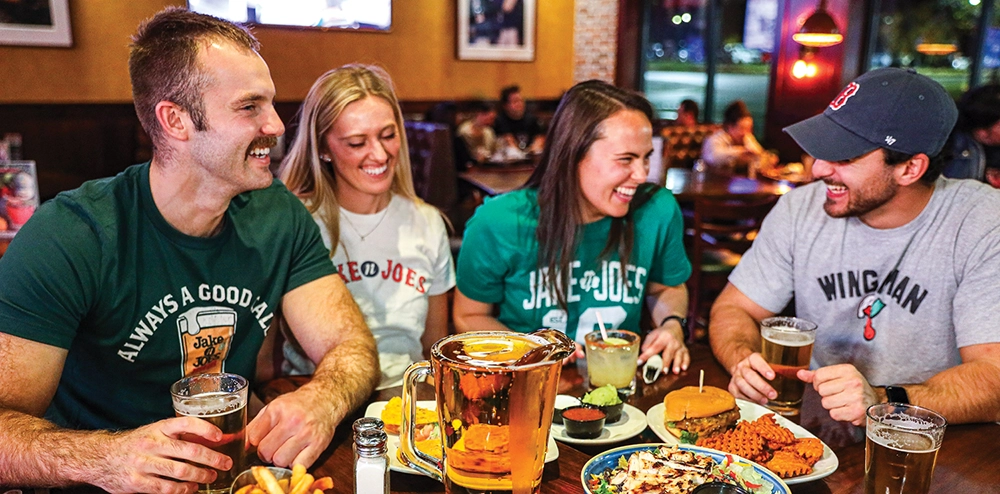 2 young men and 2 young women all wearing Jake n Joes t-shirts enjoying food, beer and cocktails